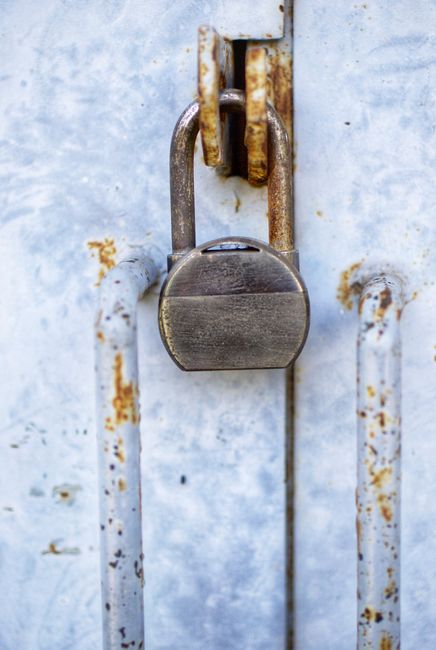 A person wearing a dark blue shirt with white polka dots is holding a white cloth and wiping the metallic door handle of a wooden door, which is part of a door lock mechanism. The door has a natural wood finish, and the metallic lock and handle appear shiny and well-maintained. The scene suggests surface cleaning focused on hygiene and sanitisation, possibly related to maintaining cleanliness for residential or commercial environments, as part of deep cleaning services offered by Enfield Carpet Cleaning. The lighting is natural, highlighting the smooth texture of the wood and the shiny surface of the lock and handle.