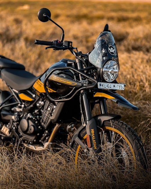 A close-up view of a black and yellow motorcycle parked in a field of dry grass during daylight. The motorcycle features a large windshield, round headlight, and a comfortable seat with visible engine components. The surface of the motorcycle is clean and well-maintained, with the branding and details clearly visible. In the background, an open landscape with golden-brown grass stretches into the distance under natural outdoor lighting. The scene captures the sleek design and shine of the motorcycle, emphasizing its condition and aesthetic appeal, relevant to surface cleaning and maintenance topics discussed by Enfield Carpet Cleaning on their website.